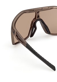 Gafas de sol marrones con un diseño moderno, que presentan lentes grandes y oscuras y una mezcla de texturas mate y brillantes en la montura. Patillas elegantes y deportivas.