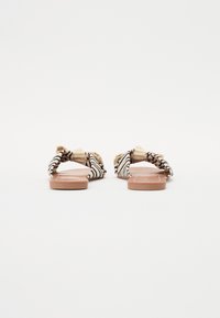 Åpne sandaler med en knyttet overdel av svart og hvitstripet stoff, tan gummisåle og flat design, som viser en minimalistisk estetikk.