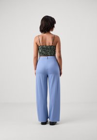 Svart blommig crop top med tunna axelband, kombinerat med högmidjade, vida ljusblå byxor; slät textur och åtsittande midjeband.