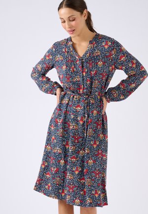 Bloemenjurk tot de knie in donkerblauw met rode en crèmekleurige patronen. Heeft lange mouwen, een knoopsluiting bij de hals en een ceintuur om de taille.