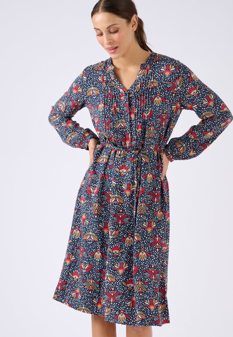 Abito lungo fino al ginocchio a fiori di colore blu scuro con motivi rossi e crema. Presenta maniche lunghe, scollatura con bottoni e vita con cintura.