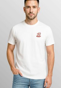 Weißes T-Shirt mit kurzen Ärmeln, das ein rotes Grafikdesign auf der linken Brust zeigt. Es besteht aus Baumwollstoff, hat einen Rundhalsausschnitt und eine lockere Passform.
