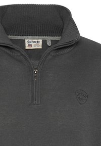 Szary dzianinowy sweter z wysokim kołnierzem, przednim zamkiem błyskawicznym i wytłoczonym logo na klatce piersiowej. Teksturowana tkanina z prążkowanym kołnierzem i mankietami.