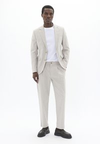 Traje de rayas en gris claro con blazer de un solo botón, pantalones de frente plano, combinado con una camiseta blanca y zapatos negros.