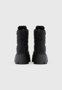 Botas negras hasta el tobillo con un material texturizado, cuello elástico y suela de goma gruesa. Presenta un patrón ondulado en la suela para mayor tracción.