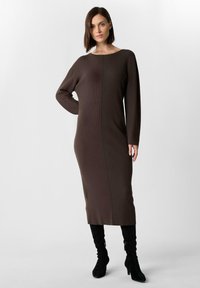 Braun gestreiftes Strickkleid mit langen Ärmeln und rundem Ausschnitt, mit einer Mittelnaht, kombiniert mit schwarzen kniehohen Stiefeln.