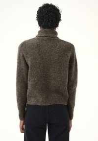 Brauner, strukturierten Pullover mit hohem Rollkragen, gerippten Bündchen und Saum. Getragen mit dunklen Jeans, von hinten gesehen vor einem schlichten Hintergrund.