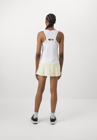 Top blanco sin mangas con un detalle de espalda abierta, combinado con una falda deportiva amarilla y zapatillas negras. Diseñado para ropa activa.