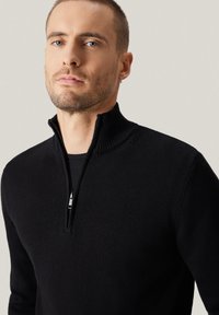 Czarny sweter z dzianiny z zamkiem i stójką. Charakteryzuje się wysokim kołnierzem oraz ozdobnym zamkiem, gładką fakturą i dopasowanym krojem.