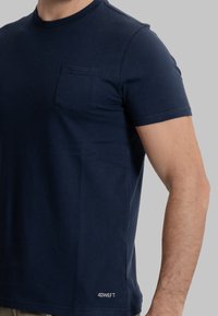 T-shirt a maniche corte blu navy in cotone, con taschino frontale e piccolo logo bianco all'orlo. Texture liscia e design aderente.