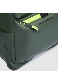 Bolsa de viaje verde con superficie texturizada, con cremallera de neón amarillo y logo de la marca. Base moldeada para mayor estabilidad.