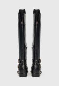 Botas de cuero negro hasta la rodilla que presentan una punta cerrada, dos hebillas decorativas y una textura suave con un ligero brillo.