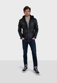 Černá kožená bunda s kapucí, se zipem vpředu a dvěma kapsami na prsou. Nositá přes šedou košili, v kombinaci s tmavými džíny a černými teniskami.