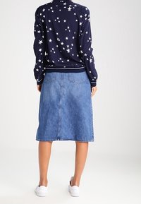 Marinblå tröja med vitt stjärnmönster, kombinerad med en ljusblå denimkjol. Modellen bär vita sneakers, vilket visar upp en avslappnad, lager-på-lager-outfit.