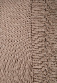 Stickad tröja i en ljus beige färg med ett strukturerat mönster på ena sidan och en slät ribbad sektion på den andra.