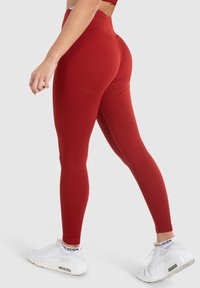Rote gerippte Leggings mit hohem Taillenanschnitt, kombiniert mit weißen Sport Sneakers. Die Leggings bieten eine enganliegende Passform und eine glatte Struktur.