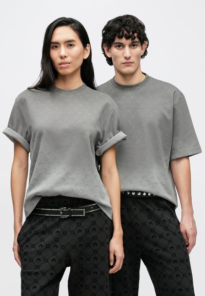 Szare t-shirty z podwiniętymi rękawami i subtelnymi wzorami, zestawione z czarnymi spodniami w wzory i paskiem z ćwiekami, prezentowane na dwóch modelkach.