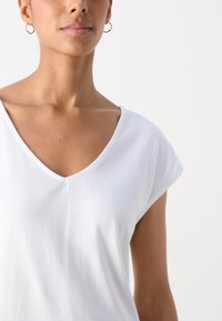 Biała koszulka z dekoltem w serek i krótkimi, podwiniętymi rękawami, wykonana z miękkiego materiału. Gładka tekstura, z minimalnymi szwami wokół dekoltu.
