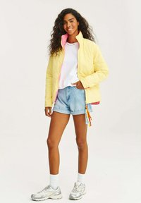 Prošívaná žlutá bunda s růžovou podšívkou, v kombinaci s bílým tričkem a světlými modrými džínovými šortkami. Obsahuje barevné táhla zipu. Stříbrné tenisky.