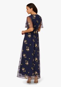 Navy Maxi-Kleid mit floralem Stickerei, durchsichtigen Ärmeln und geknotetem Taillen-Detail. Der Stoff hat eine fließende Textur und ein dezentes Blumenmuster.