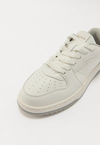Light gray sneaker with a smooth leather upper, round toe, perforated detailing, and a textured rubber sole. Features a lace-up design and logo.
