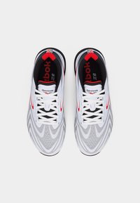 Λευκά και γκρι παπούτσια τρεξίματος Reebok με κόκκινες λεπτομέρειες, δεμένα με κορδόνια, σε θέα από πάνω σε απλό λευκό φόντο.