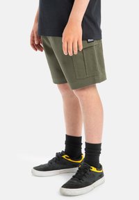Gröna bomullsshorts med rak passform, utrustade med sidofickor och en fållkant, kombinerade med svarta sneakers och svarta strumpor.