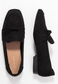 Ballerines en daim noir avec un détail en nœud à l'avant, forme de bout carré et petit talon bloc noir. Logo embossé sur la semelle intérieure.