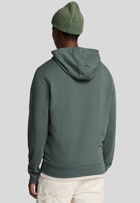 Donkergroene katoenen hoodie met een kangoeroezak, ribgebreide manchetten en zoom, met een gladde textuur. Draagt een bijpassende beanie.