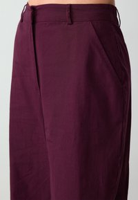 Bordeauxkleurige broek van gemêleerd stof, met een rechte pasvorm, zijzakken en een schone tailleband met riemlussen.
