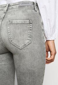 Jeans de ganga cinza com um design ajustado, apresentando um bolso traseiro e uma etiqueta com a inscrição "ONLY". O material parece suave com uma textura lisa.