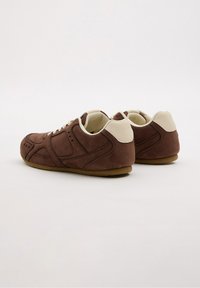 Zapatillas de ante marrón con un talón y un cuello de un tono beige claro, que presentan un diseño texturizado y cierre con cordones. Suela de goma sólida para mayor tracción.