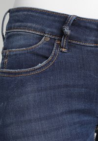 Jeans de mezclilla azul oscuro con un diseño clásico, costuras naranjas, un bolsillo frontal y un detalle de lazo anudado en el cinturón.