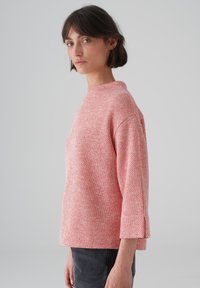 Top a righe rosse e bianche in maglia con scollatura alta, maniche lunghe fino al gomito e vestibilità rilassata. Tessuto testurizzato con un motivo sottile.