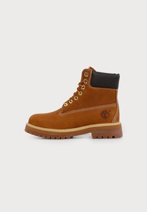 Bottine en cuir marron avec col rembourré noir, œillets dorés, semelle épaisse à crampons et logo Timberland sur le côté du talon.