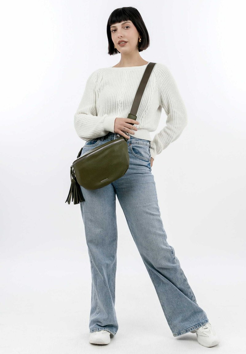 Olive green leather shoulder bag with a textured surface, zipper closure, and decorative tassels, worn with light blue flared jeans.