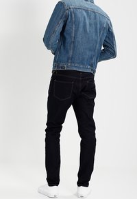 Světle modrá džínová bunda v kombinaci s tmavě černými džínami. Na spodní části jsou vidět bílé tenisky, které doplňují jednoduchý a ležérní vzhled.