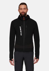Black softshell jacket with a hood, featuring a front zipper, zippered chest pockets, and textured front panels. Branding is visible on the chest.