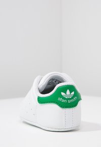 White sneaker with green accent at heel. Features smooth leather material, perforated details on side, and "Stan Smith" branding on back.