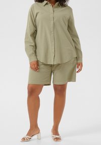 Olijfgroene overhemdbloes met bijpassende shorts, gemaakt van een zachte, gestructureerde stof. Gedragen met crème blokhakken sandalen.