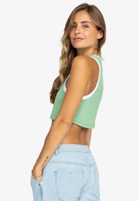 Top corto verde con ribete blanco, hecho de una tela texturizada. La modelo lleva puesto unos pantalones de mezclilla de cintura alta en color azul claro.