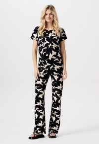 Zwart en crèmekleurig bloemenpatroon tweedelig outfit met een t-shirt met korte mouwen en wijde broekspijpen, gecombineerd met zwarte sandalen.