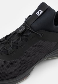 Chaussure de sport noire avec une tige en mesh, un système de laçage intégré élégant et une semelle en caoutchouc avec un motif de grip texturé.