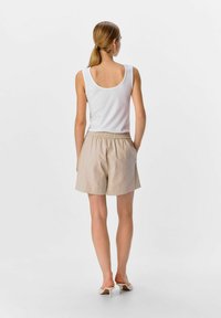 Pantaloni corti in lino beige con una cintura elasticizzata, abbinati a un top bianco aderente, che mostrano una silhouette semplice e rilassata.