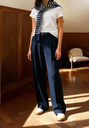 Person wearing white t-shirt, navy wide-leg trousers, striped sweater draped over shoulders, and white sneakers standing indoors near chair.