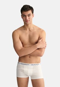 Boxerii albi cu un tiv elastic de marcă în nuanță de bleumarin. Materialul pare neted, se potrivește strâns pe corp.