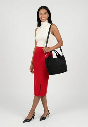 Vrouw glimlacht, draagt een witte mouwloze coltrui, rode midi-rok met een voorsplit, zwarte hakken en draagt een zwarte schoudertas.