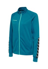 Giacca sportiva con zip color verde petrolio con colletto e polsini a coste, strisce a chevron nere e grigie sulle maniche e logo "hummel" sul petto.