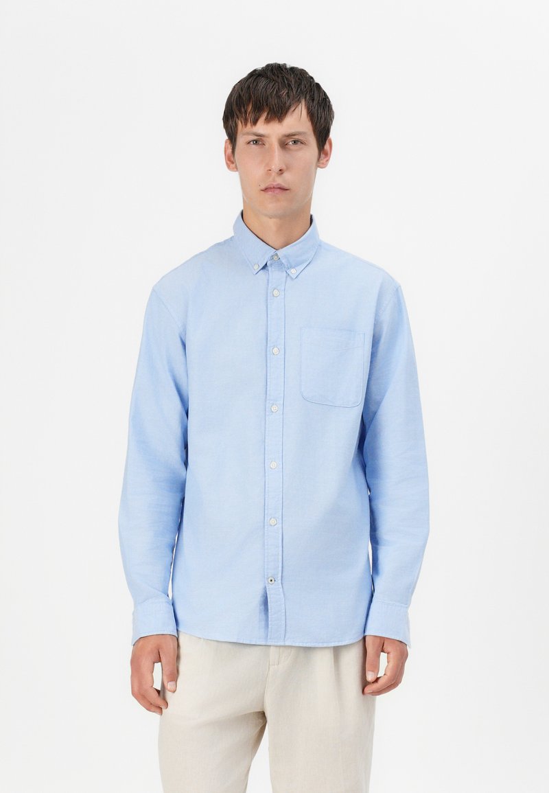 Light blue long-sleeve button-up shirt in cotton with a single chest pocket and a classic collar, featuring a smooth texture and simple design.