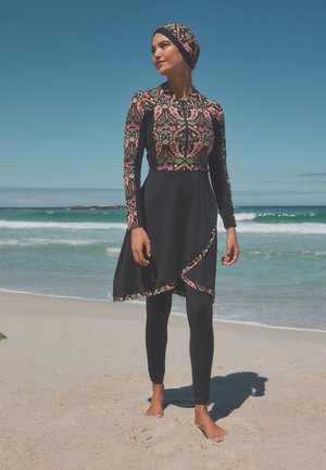Schwarze, bescheidene Bademode mit floralen Mustern auf dem Oberteil, langen Ärmeln und einem geschwungenen Saum. Enthält Leggings und eine passende Kopfbedeckung.